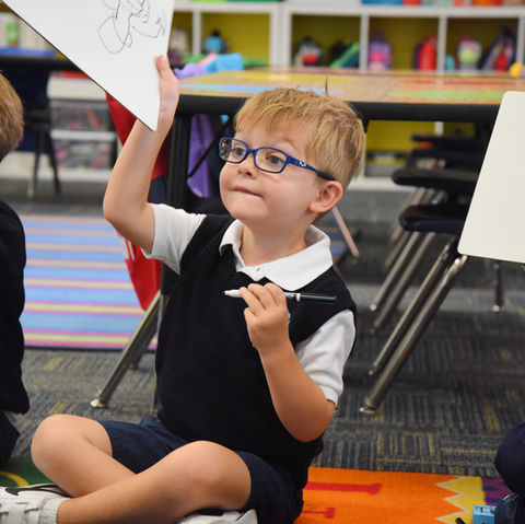 A transitional kindergarten student holds white board with drawing at Saint Nicholas Catholic School