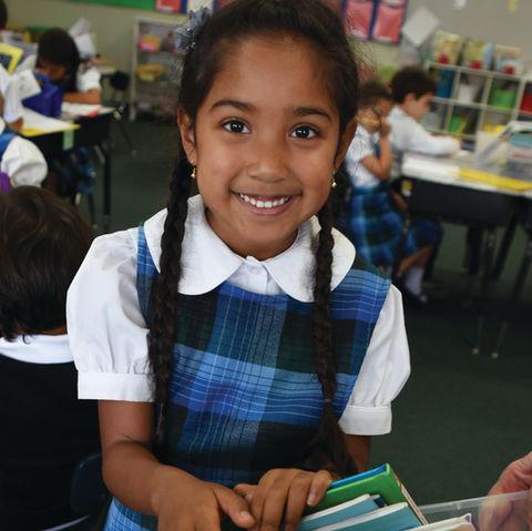 A smiling first grade student chosing a book to read from a book bin at Saint Nicholas Catholic School.